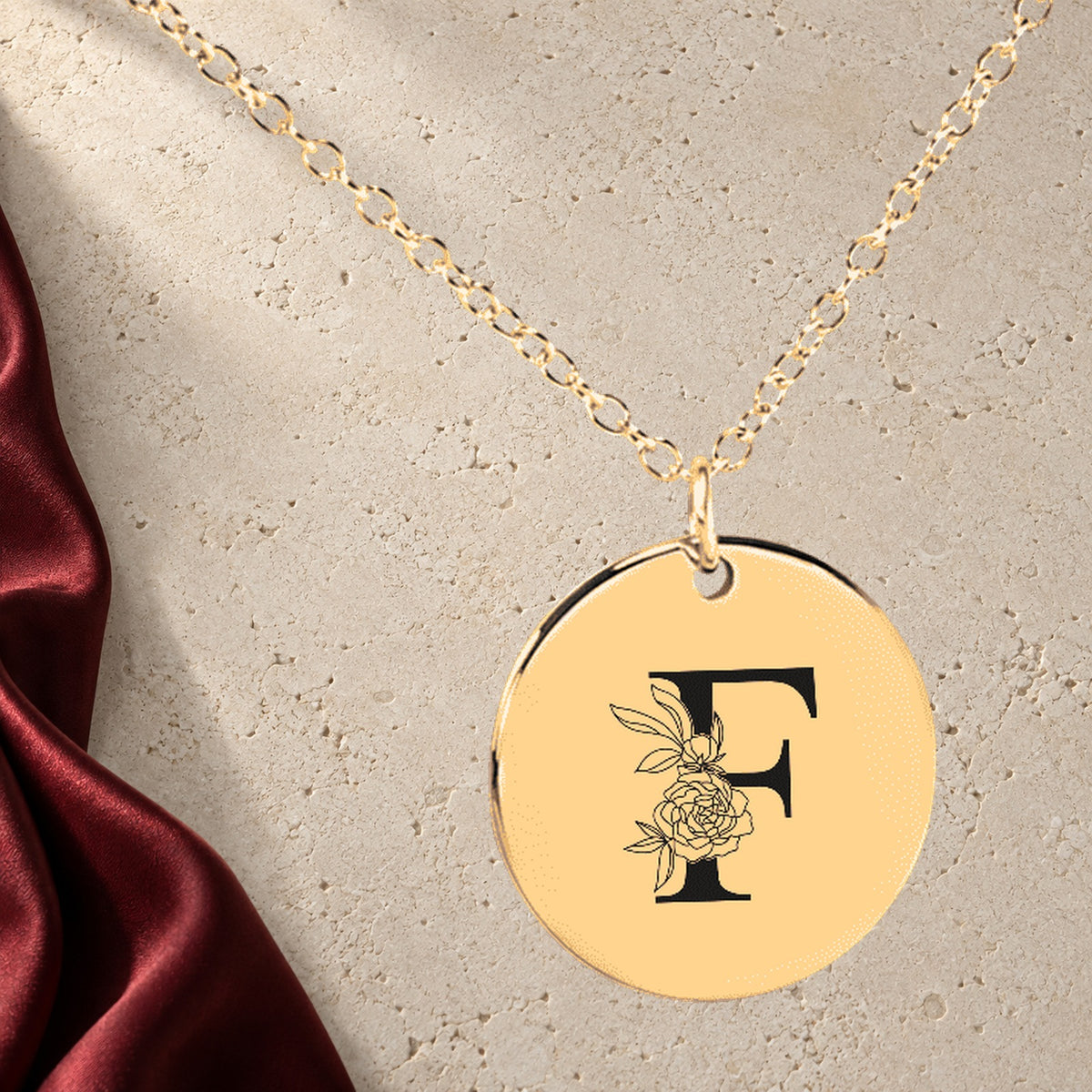 Collier Initiale Florale F Personnalisé en finition dorée sur pierre claire, avec étoffe rouge sanguine ; exemple de personnalisation.