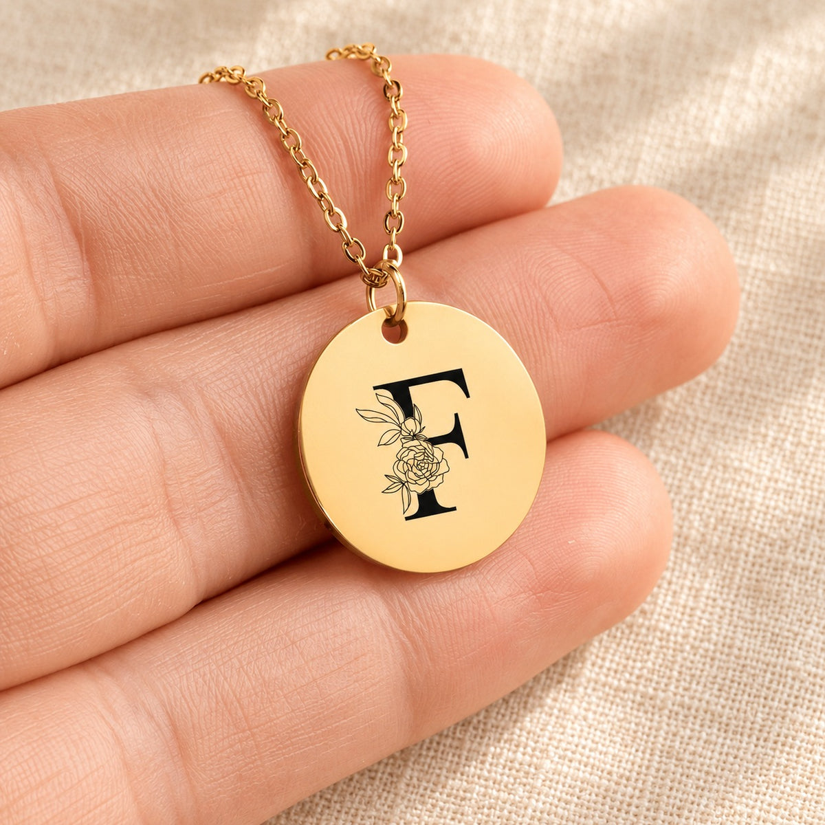 Collier initiale florale F personnalisé doré tenu en main, détail de la gravure.