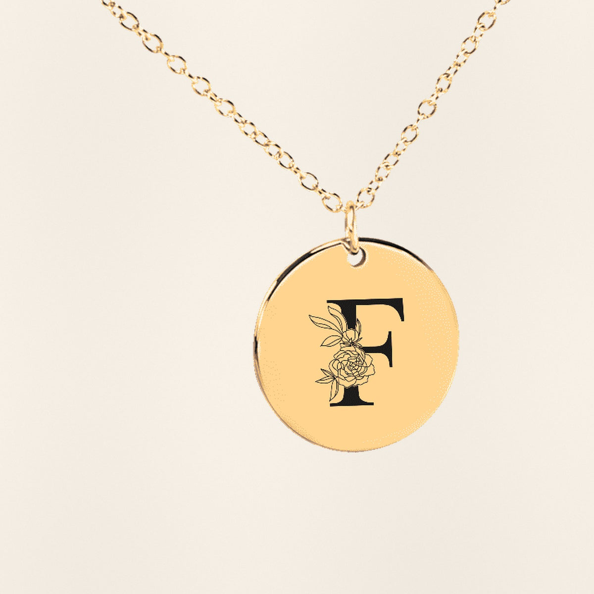 Collier Initiale Florale F Personnalisé en finition dorée, exemple de gravure sur fond ivoire texturé.