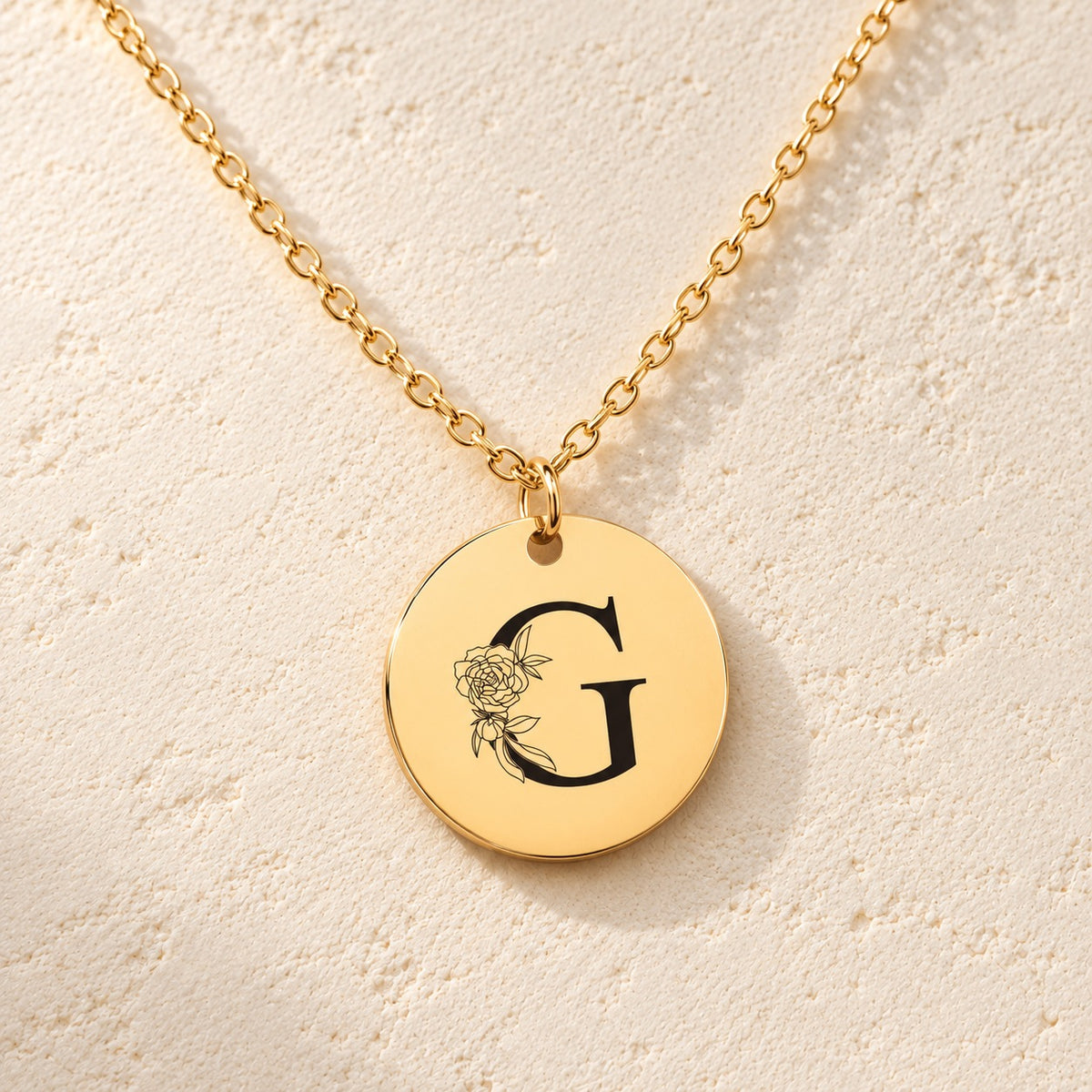 Détail de la médaille ronde dorée avec initiale G et fleurs.