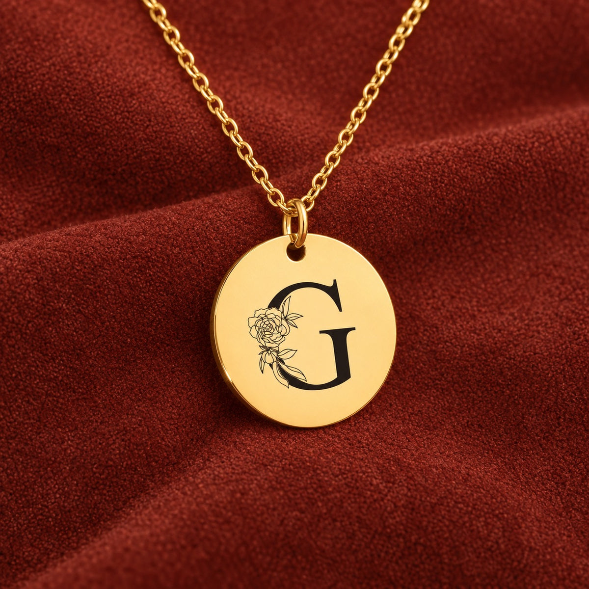 Médaille ronde dorée avec initiale G et fleurs, sur suédine rouge sanguine.