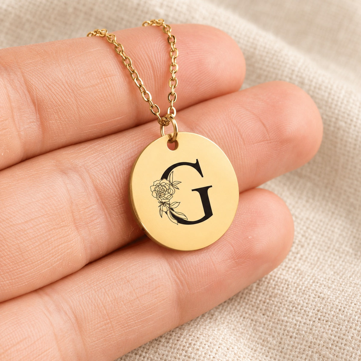 Collier initiale florale G personnalisé doré tenu en main, détail de la gravure.