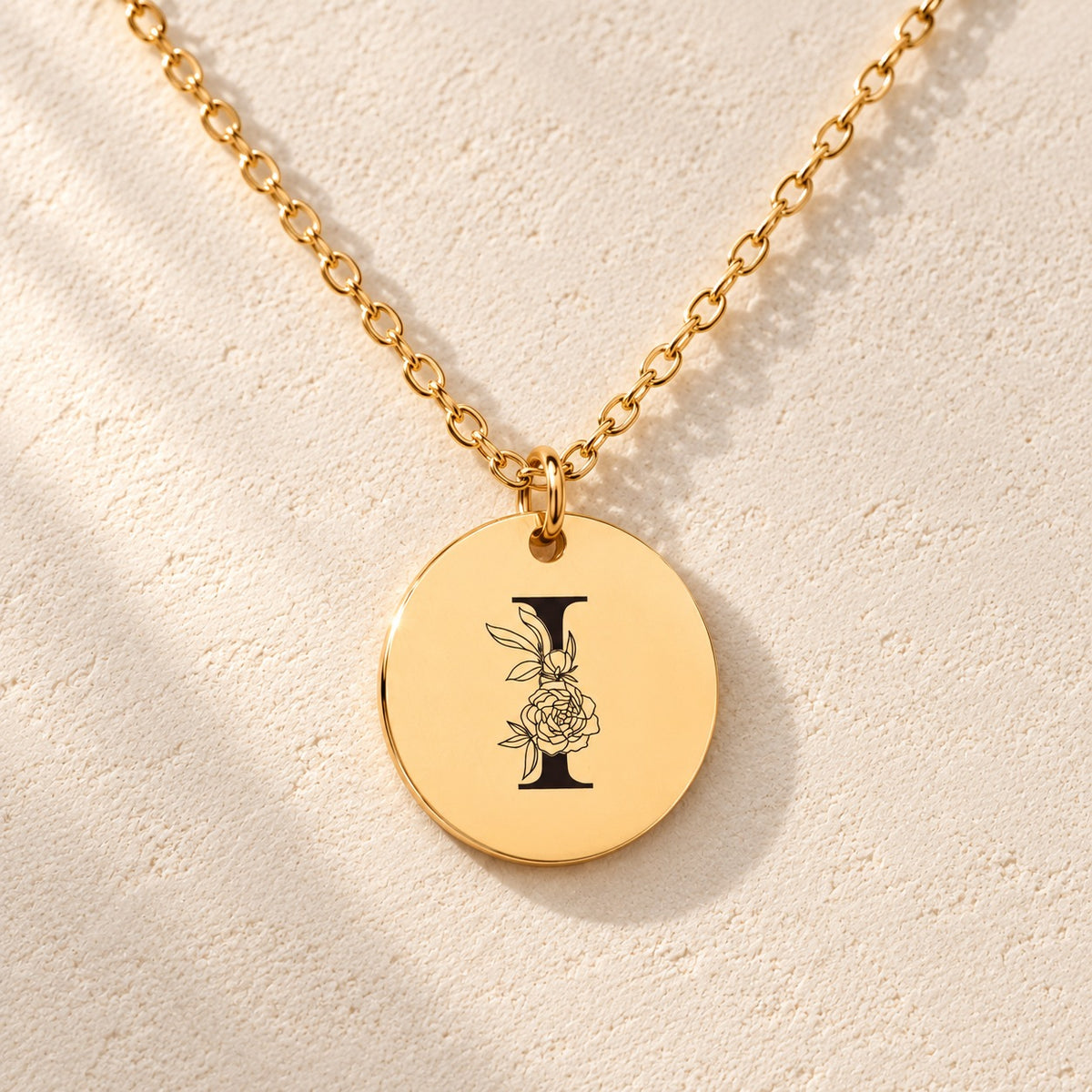 Détail de la médaille ronde dorée avec initiale I et fleurs.