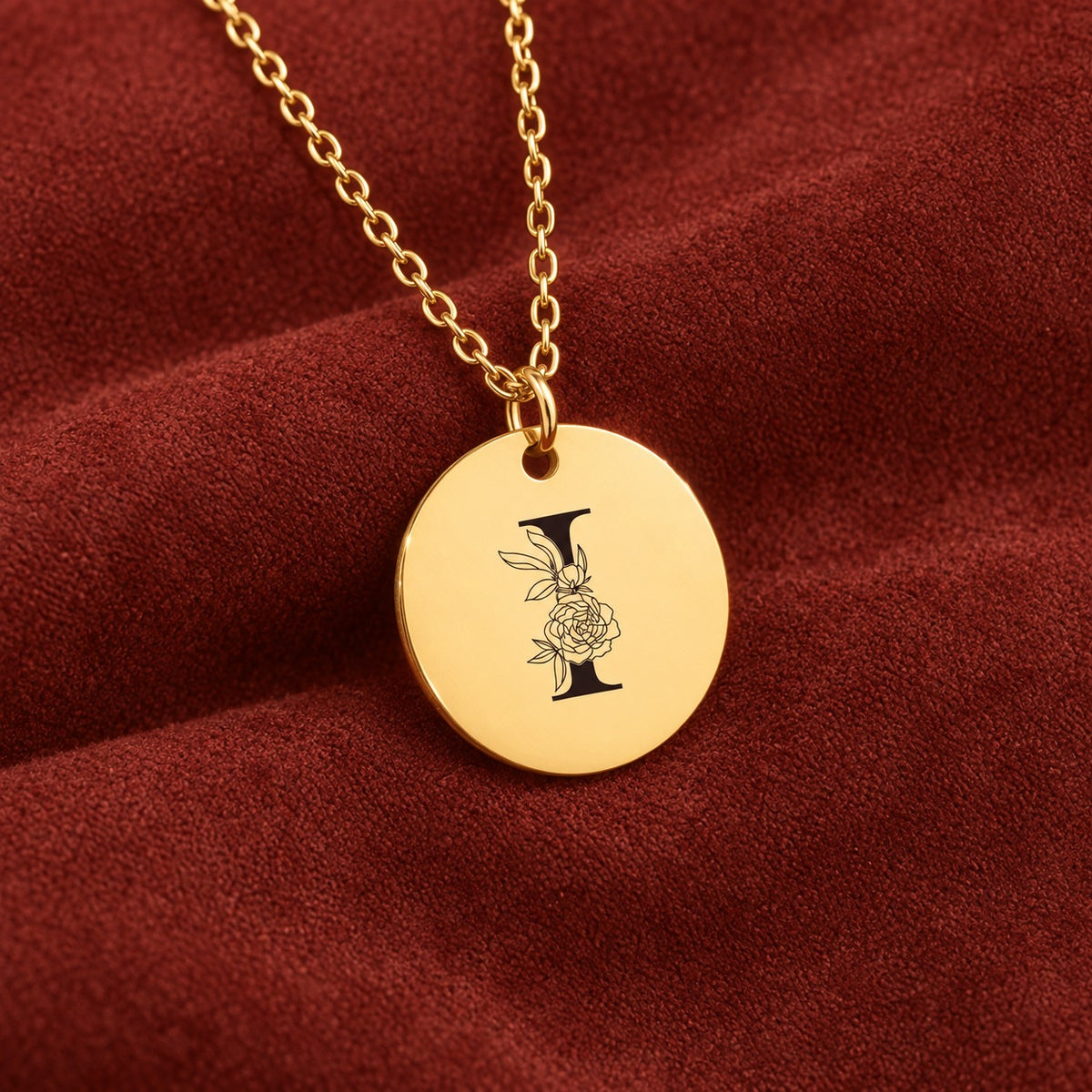 Médaille ronde dorée avec initiale I et fleurs, sur suédine rouge sanguine.