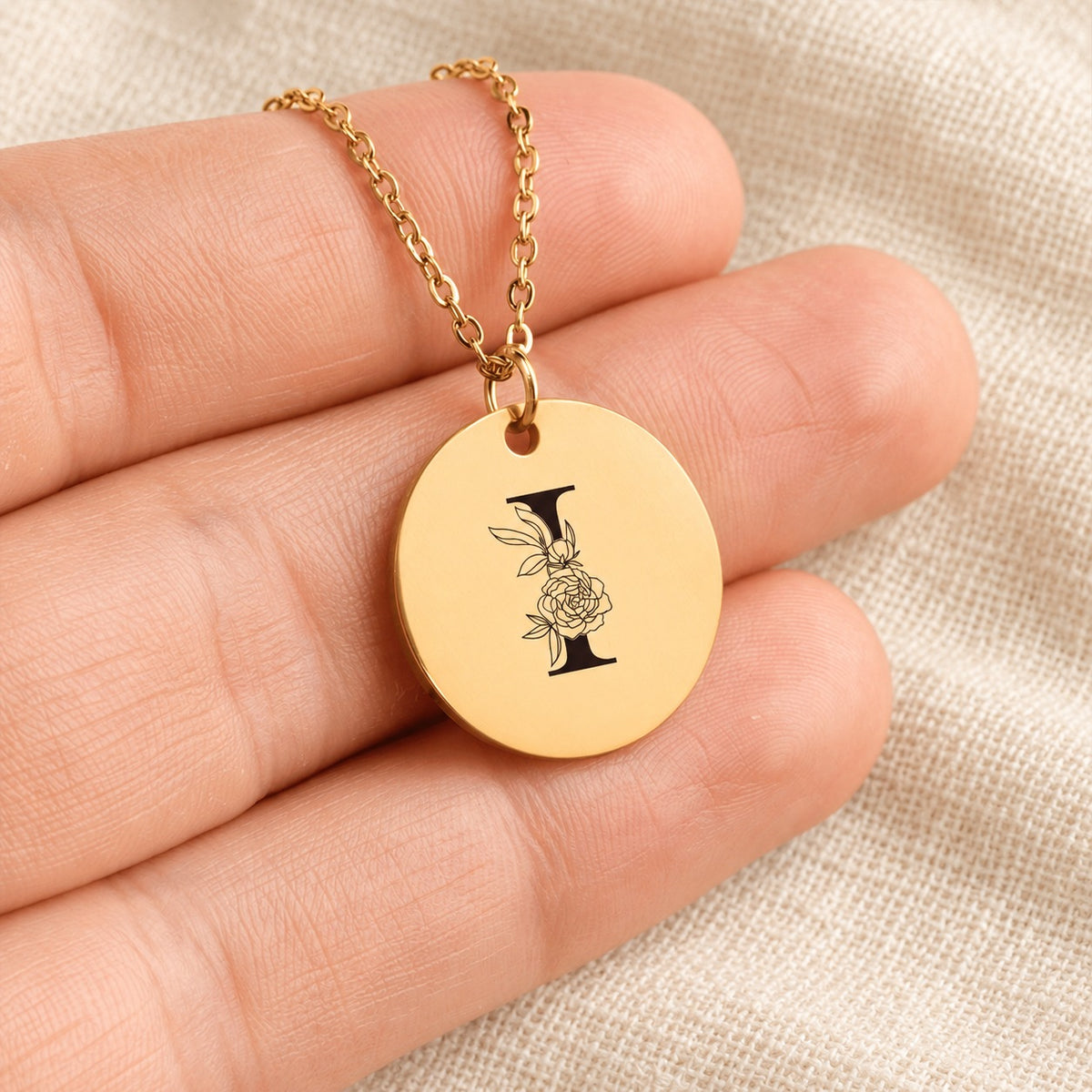 Collier initiale florale I personnalisé doré tenu en main, détail de la gravure.