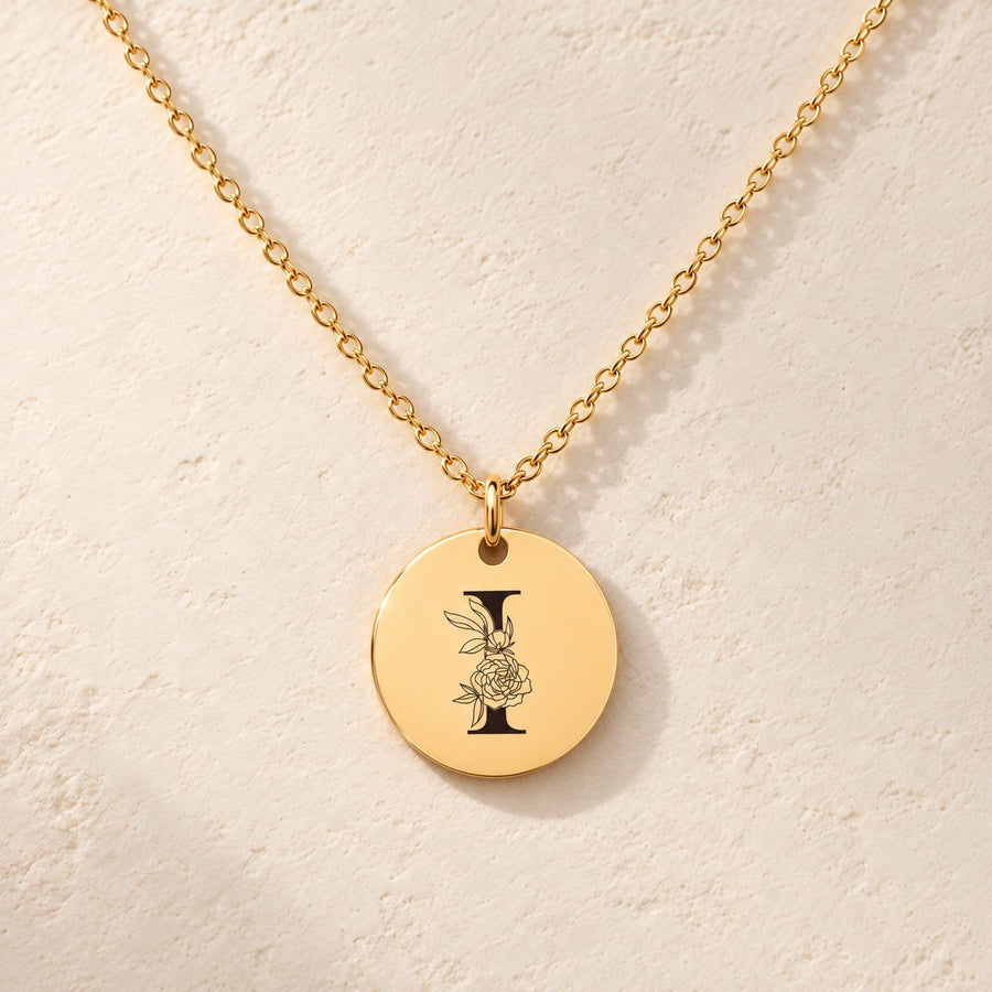 Collier initiale florale I personnalisé doré, médaille ronde gravée avec initiale I et fleurs, sur fond ivoire.