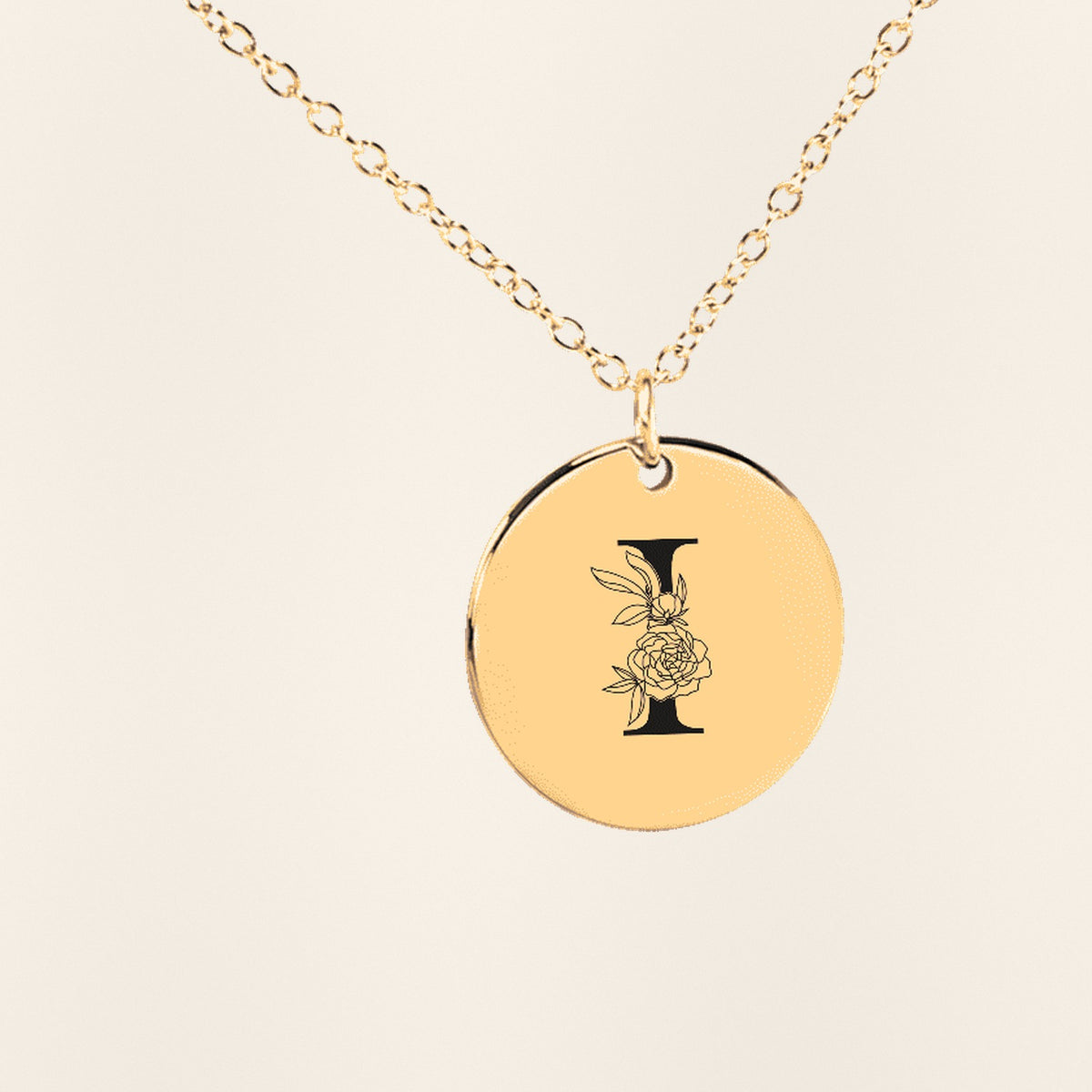 Collier Initiale Florale I Personnalisé en finition dorée, exemple de gravure sur fond ivoire texturé.