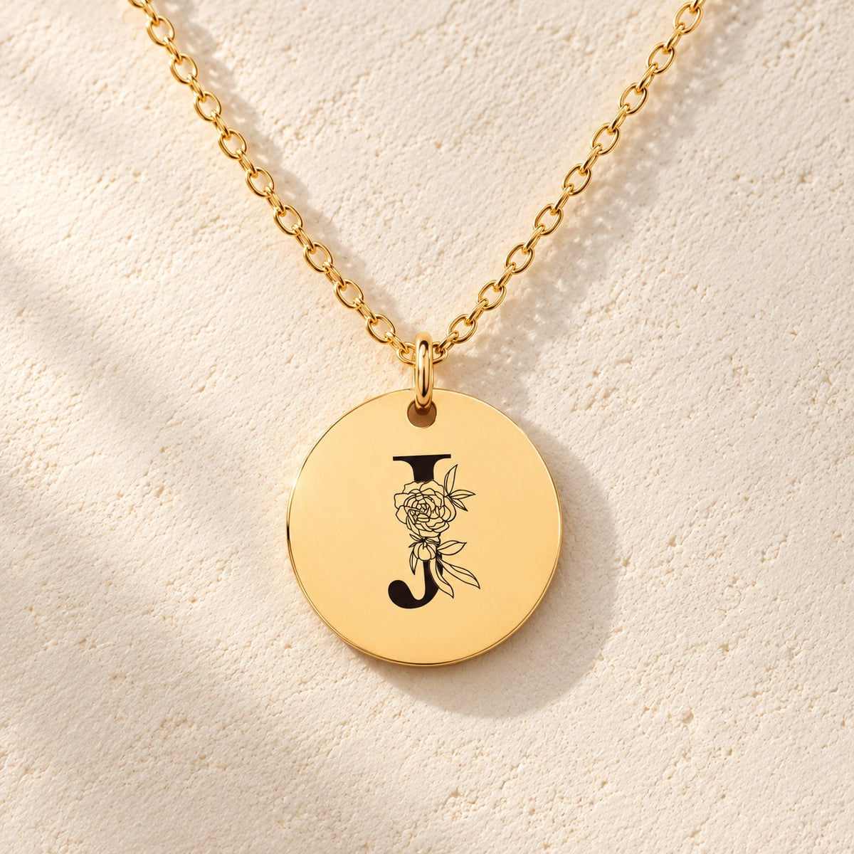 Détail de la médaille ronde dorée avec initiale J et fleurs.