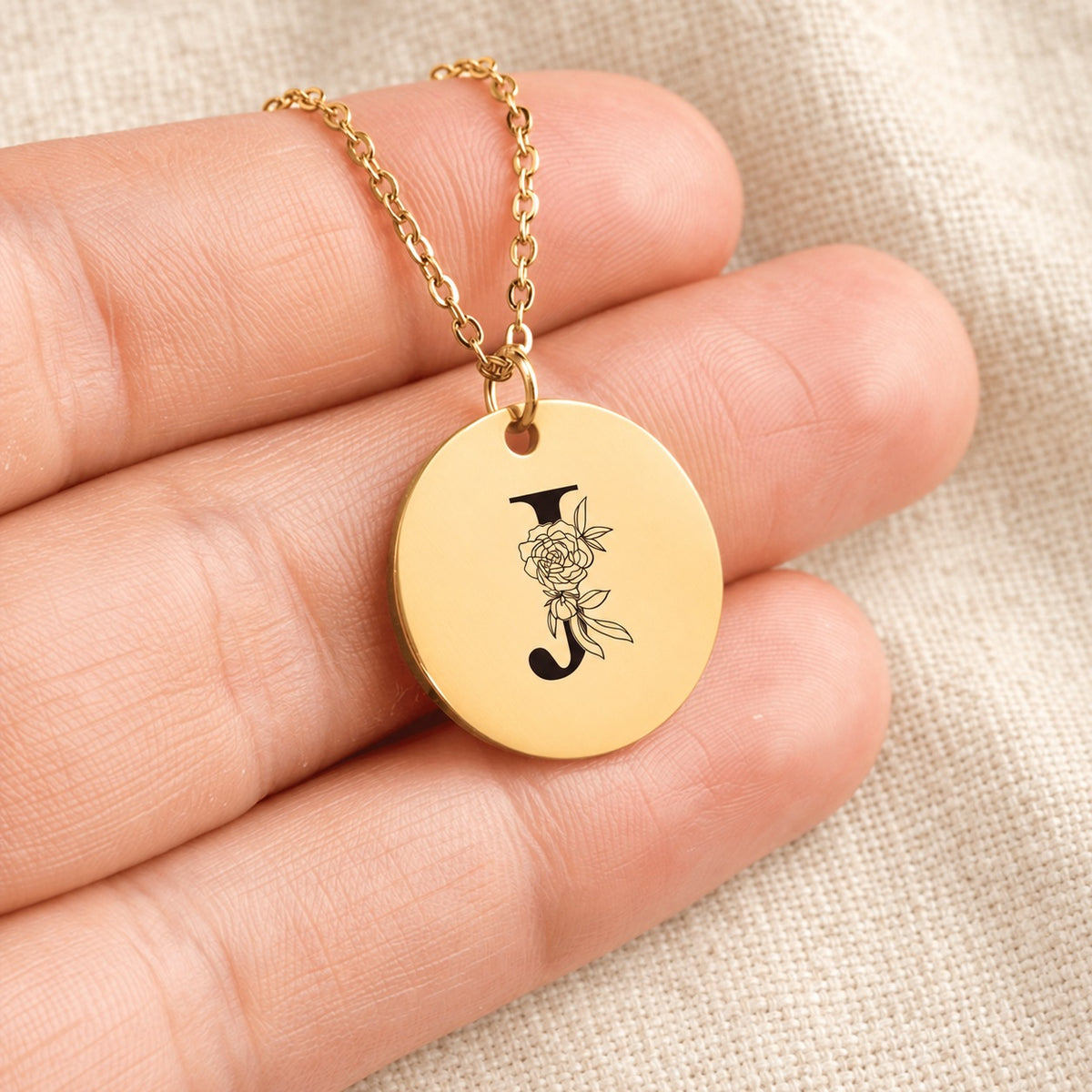 Collier initiale florale J personnalisé doré tenu en main, détail de la gravure.