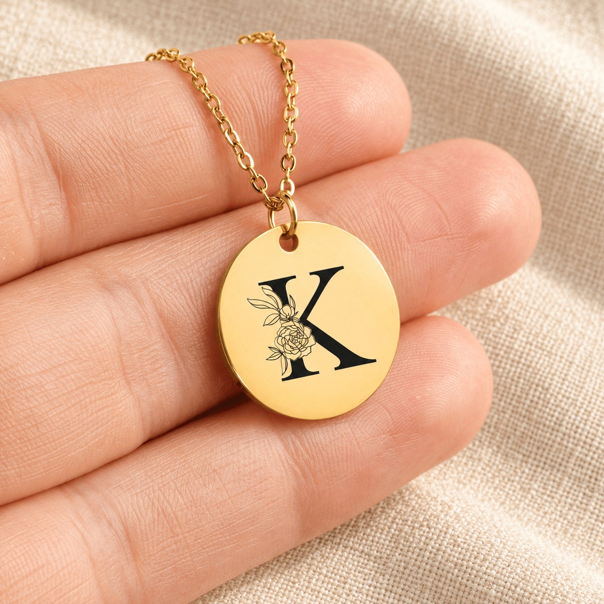 Collier initiale florale K personnalisé doré tenu en main, détail de la gravure.