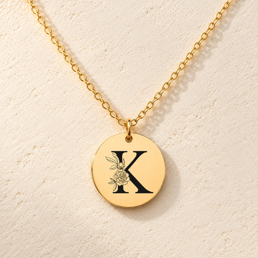 Collier initiale florale K personnalisé doré, médaille ronde gravée avec initiale K et fleurs, sur fond ivoire.