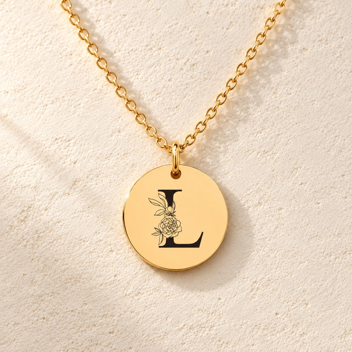 Détail de la médaille ronde dorée avec initiale L et fleurs.