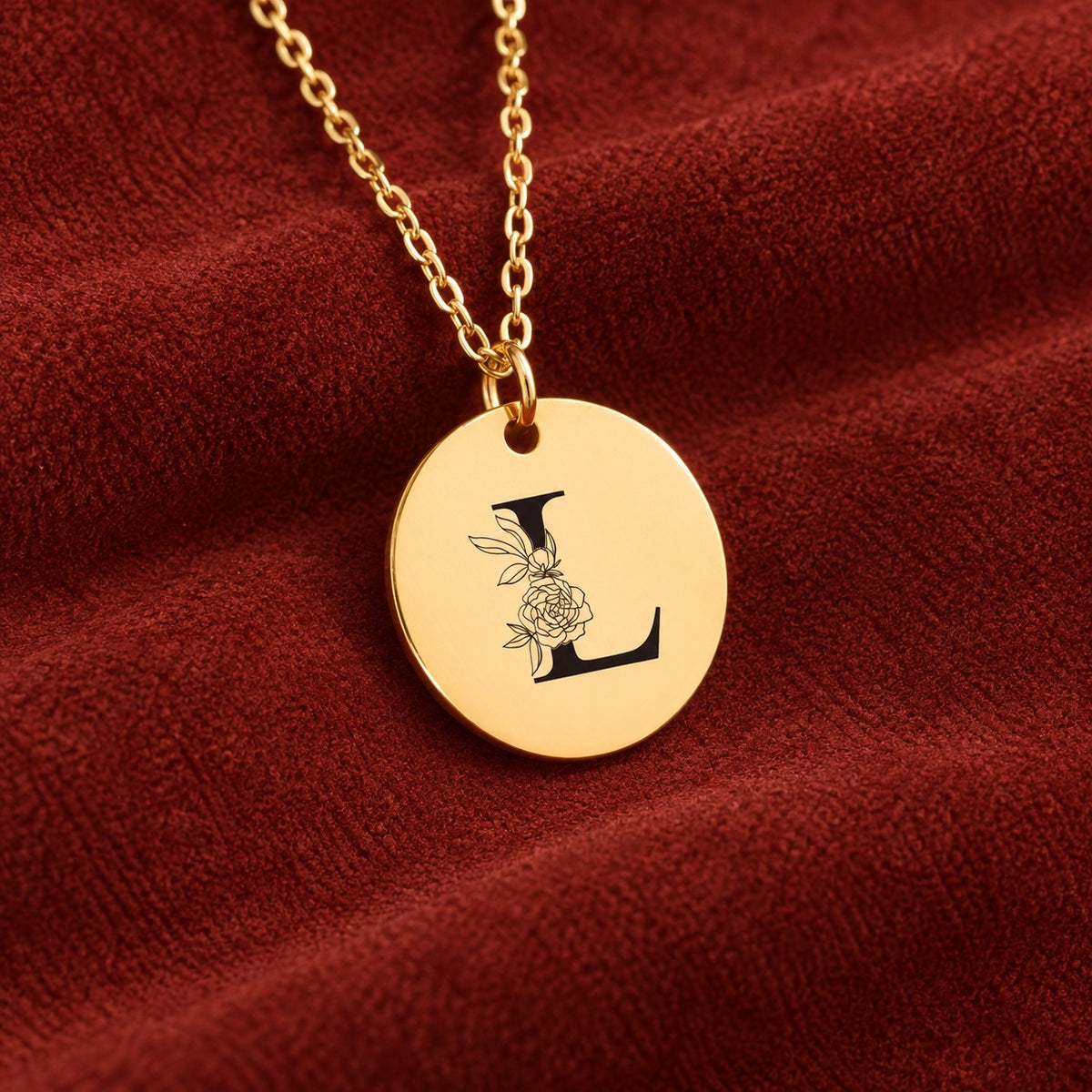 Médaille ronde dorée avec initiale L et fleurs, sur suédine rouge sanguine.