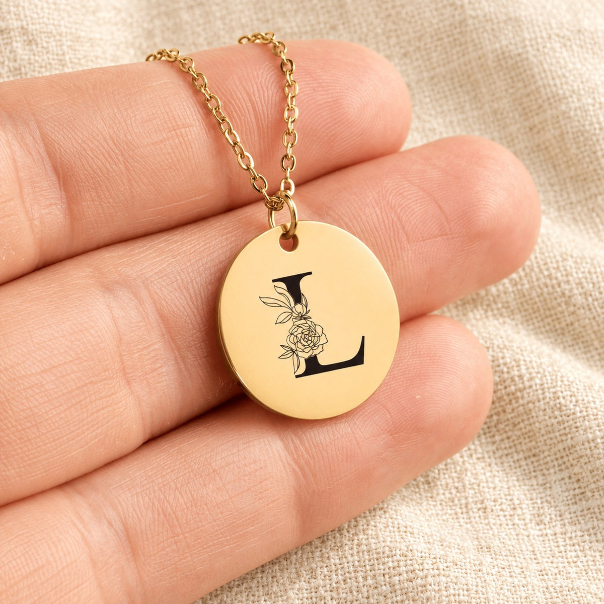 Collier initiale florale L personnalisé doré tenu en main, détail de la gravure.