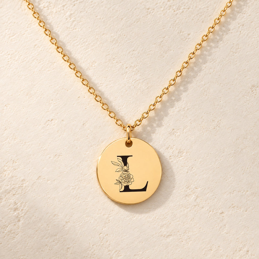 Collier initiale florale L personnalisé doré, médaille ronde gravée avec initiale L et fleurs, sur fond ivoire.