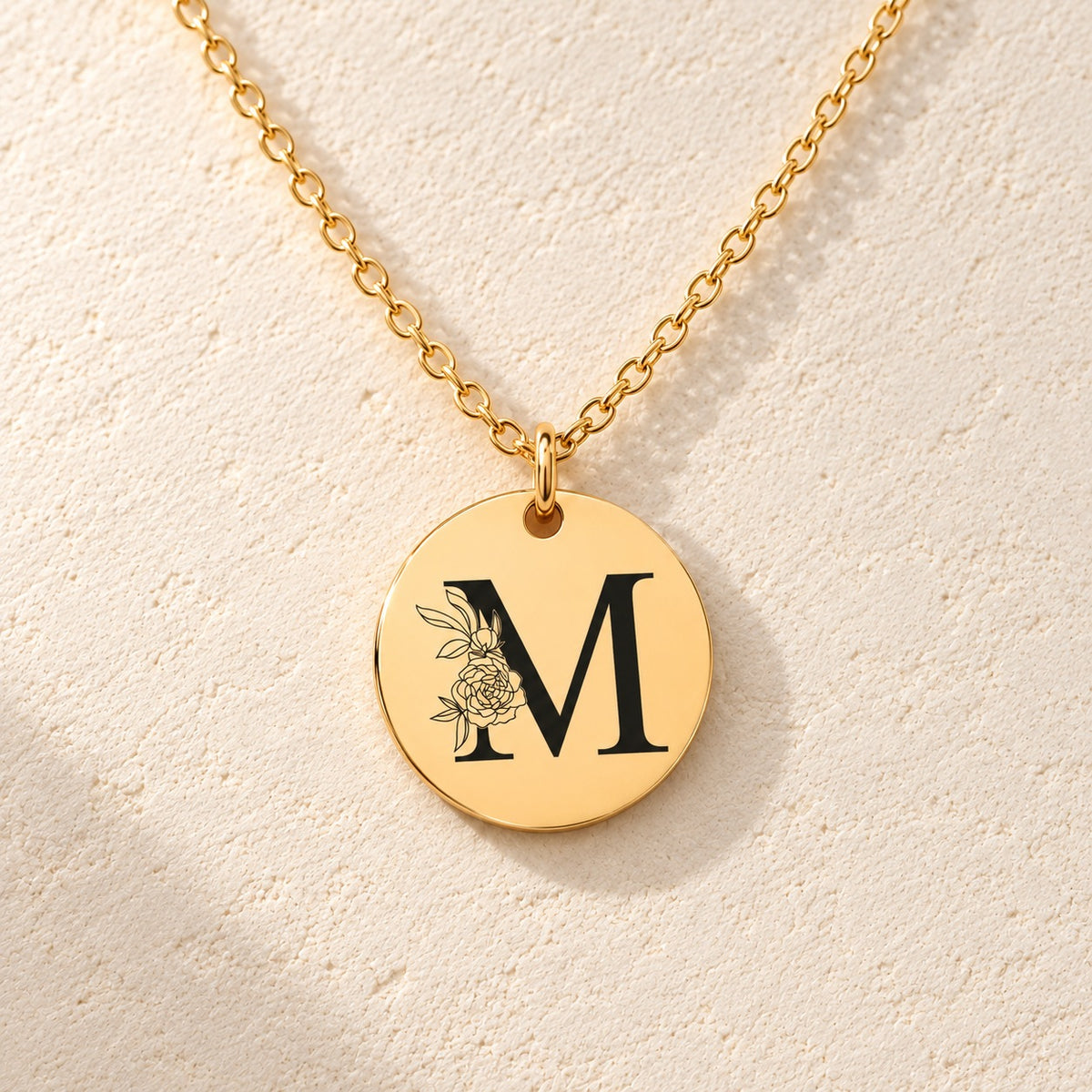 Détail de la médaille ronde dorée avec initiale M et fleurs.