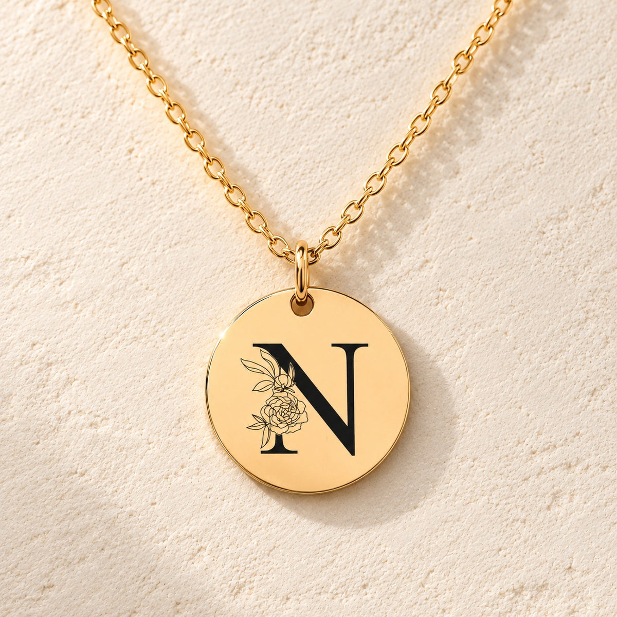 Détail de la médaille ronde dorée avec initiale N et fleurs.
