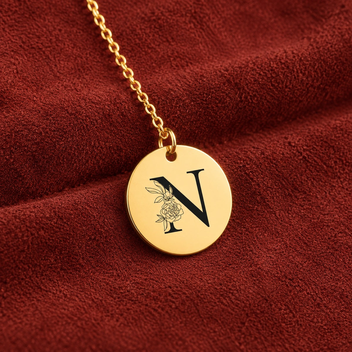 Médaille ronde dorée avec initiale N et fleurs, sur suédine rouge sanguine.