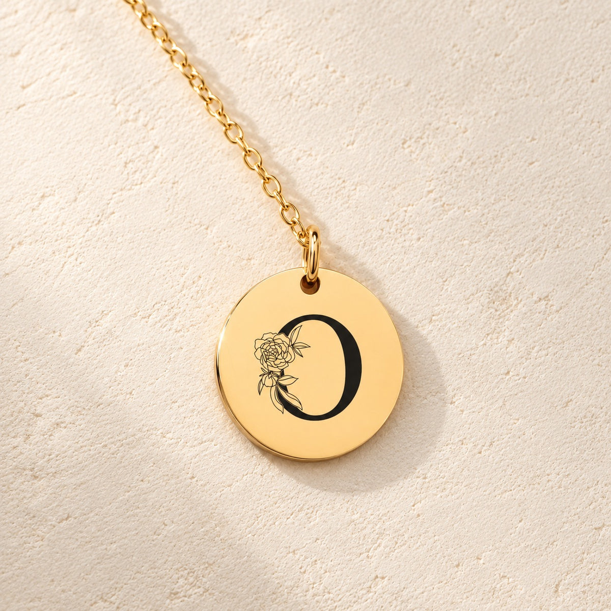Détail de la médaille ronde dorée avec initiale O et fleurs.
