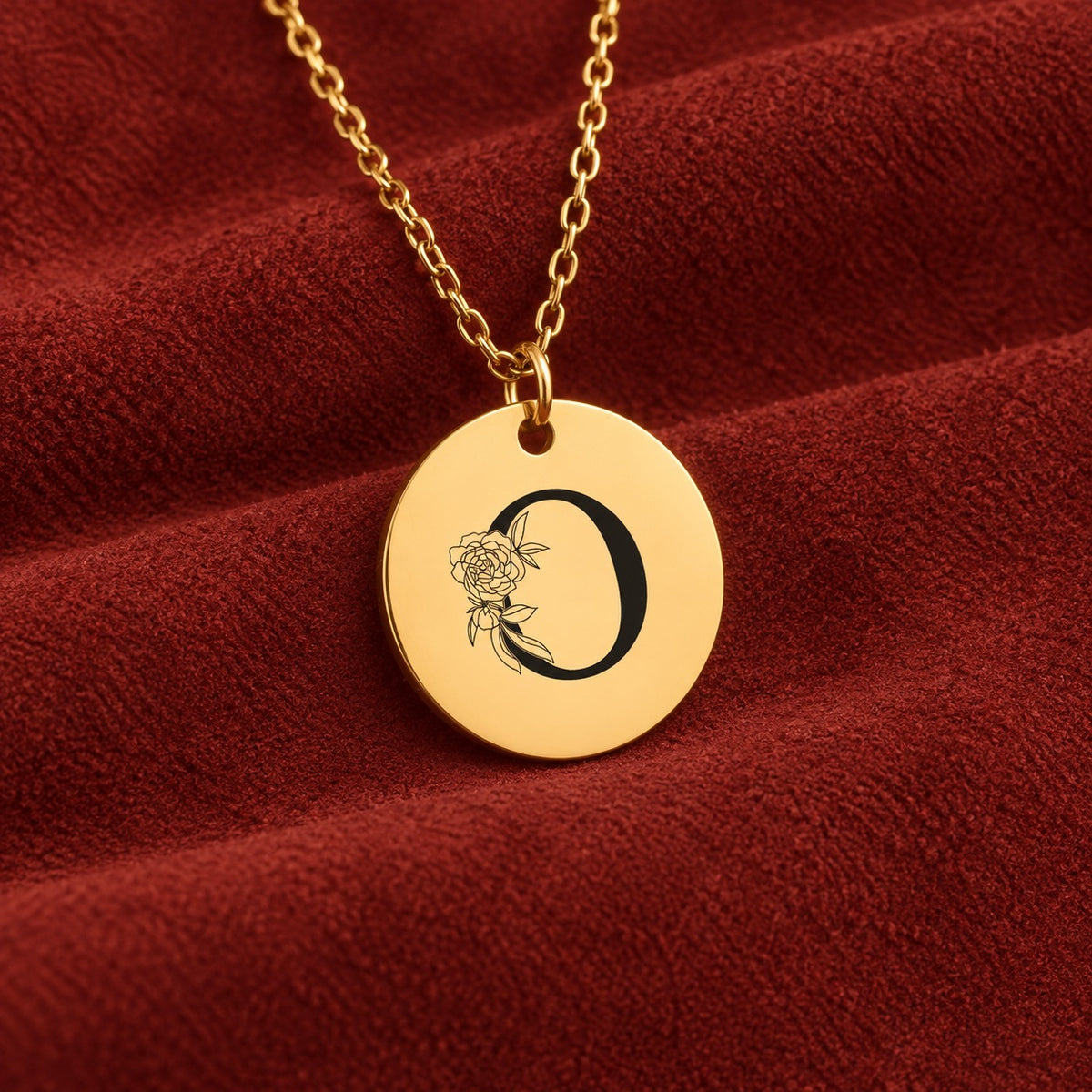 Médaille ronde dorée avec initiale O et fleurs, sur suédine rouge sanguine.