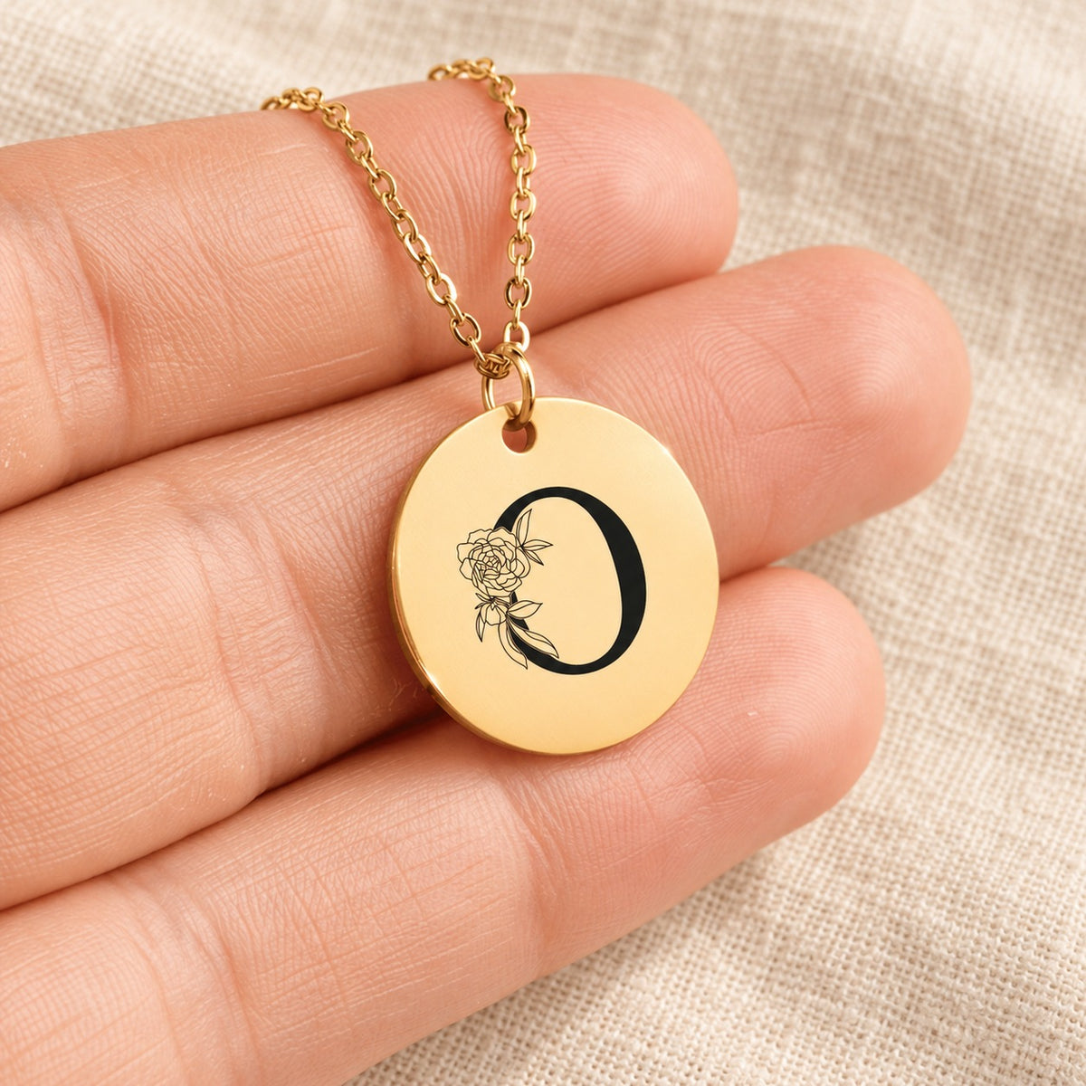 Collier initiale florale O personnalisé doré tenu en main, détail de la gravure.