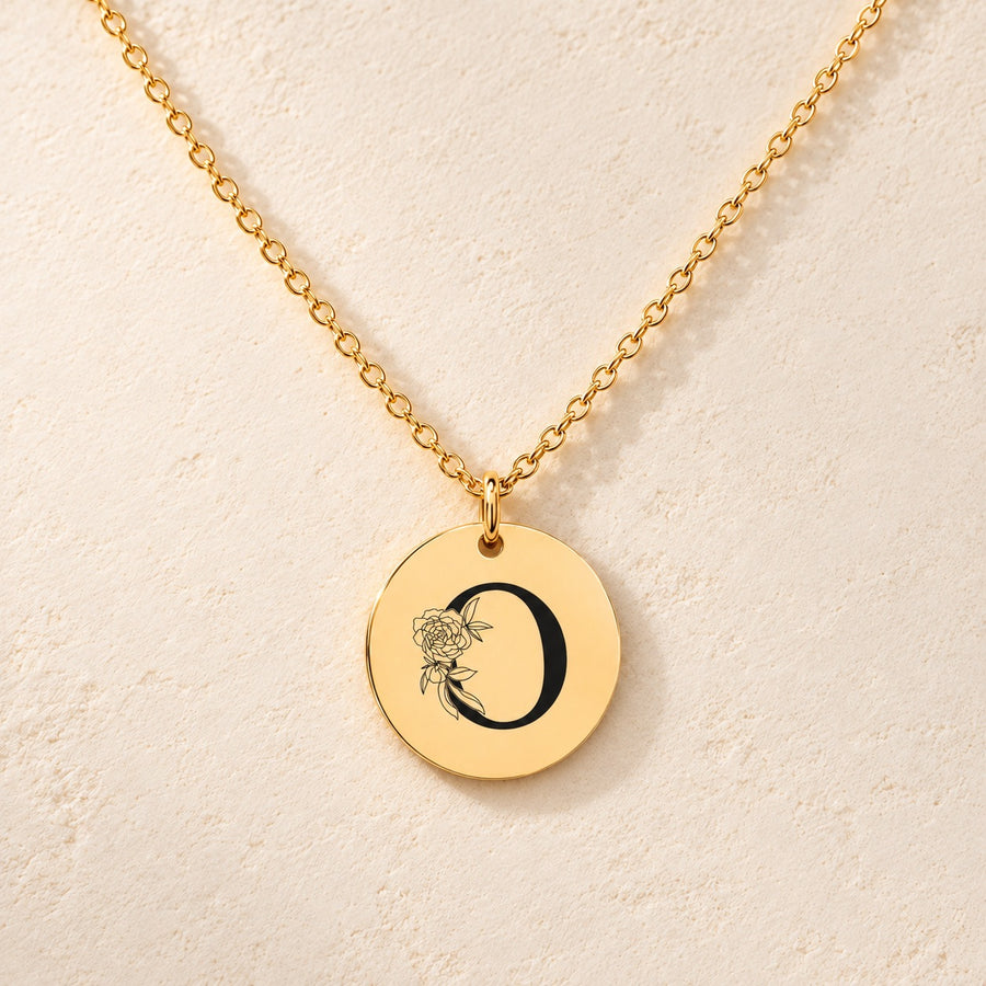 Collier initiale florale O personnalisé doré, médaille ronde gravée avec initiale O et fleurs, sur fond ivoire.