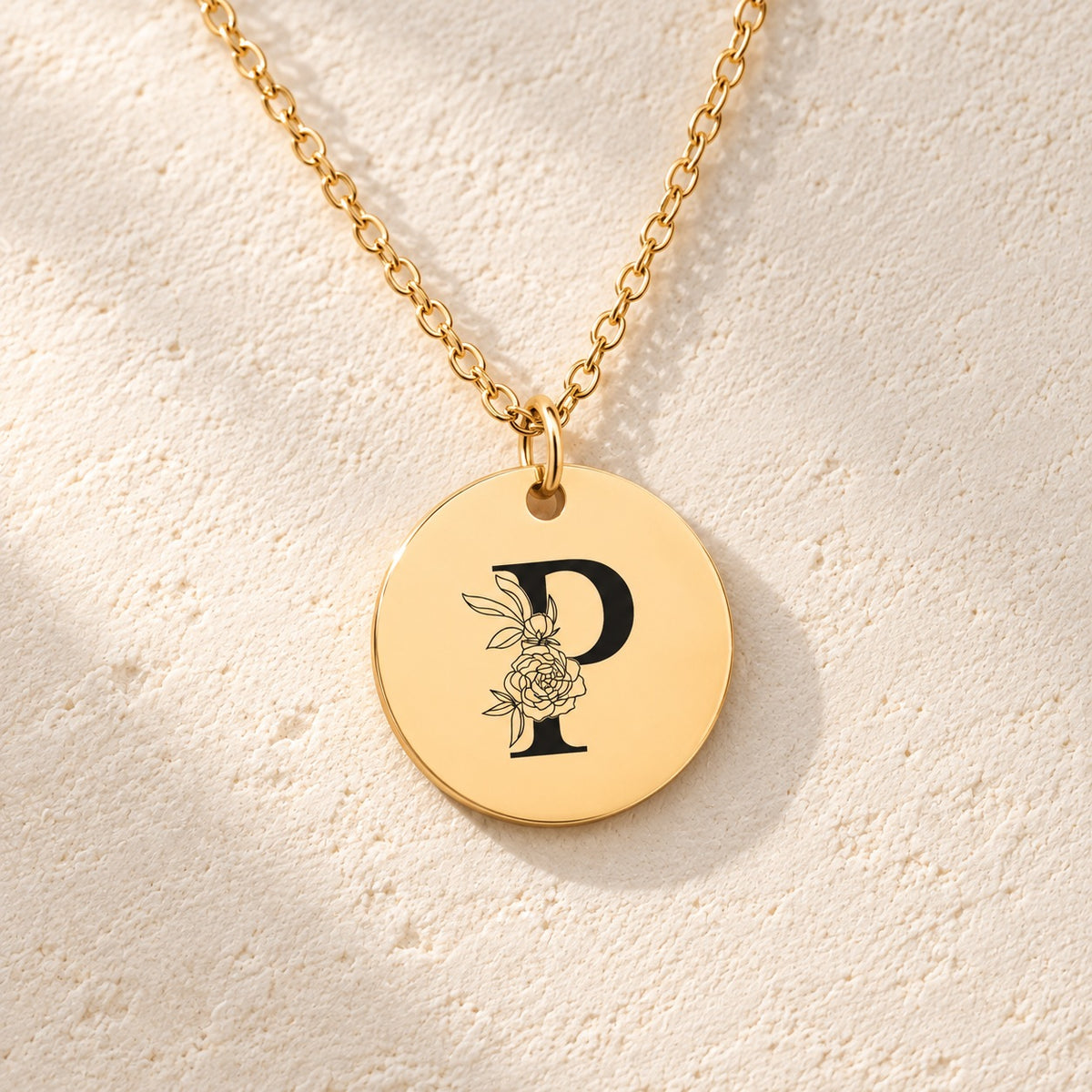 Détail de la médaille ronde dorée avec initiale P et fleurs.