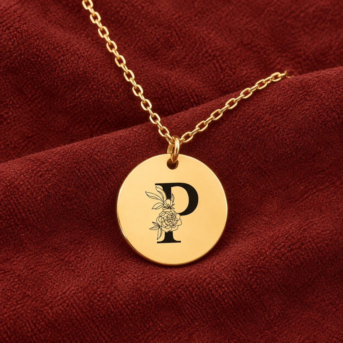 Médaille ronde dorée avec initiale P et fleurs, sur suédine rouge sanguine.