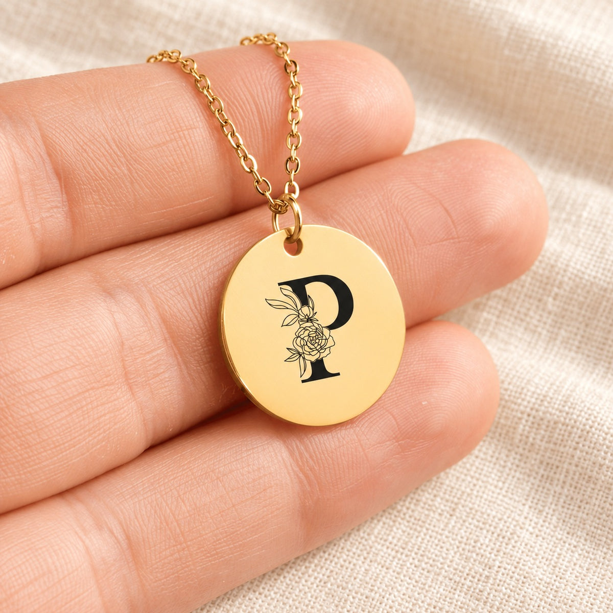 Collier initiale florale P personnalisé doré tenu en main, détail de la gravure.