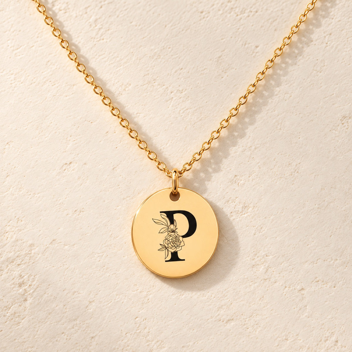 Collier initiale florale P personnalisé doré, médaille ronde gravée avec initiale P et fleurs, sur fond ivoire.