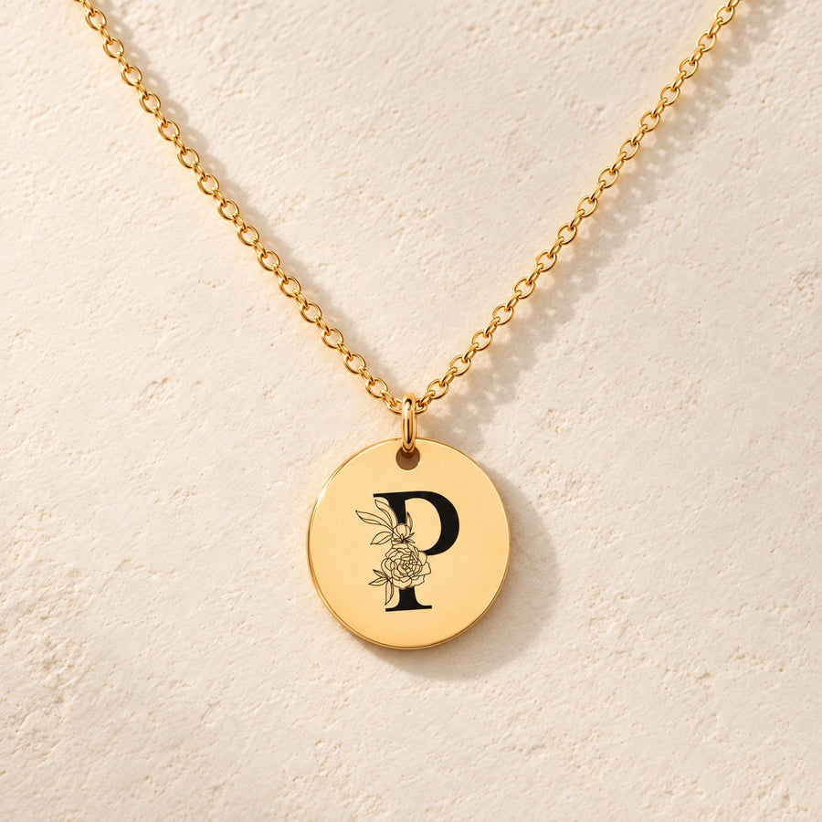Collier initiale florale P personnalisé doré, médaille ronde gravée avec initiale P et fleurs, sur fond ivoire.