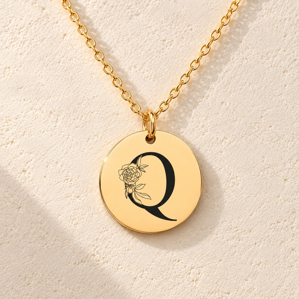 Détail de la médaille ronde dorée avec initiale Q et fleurs.