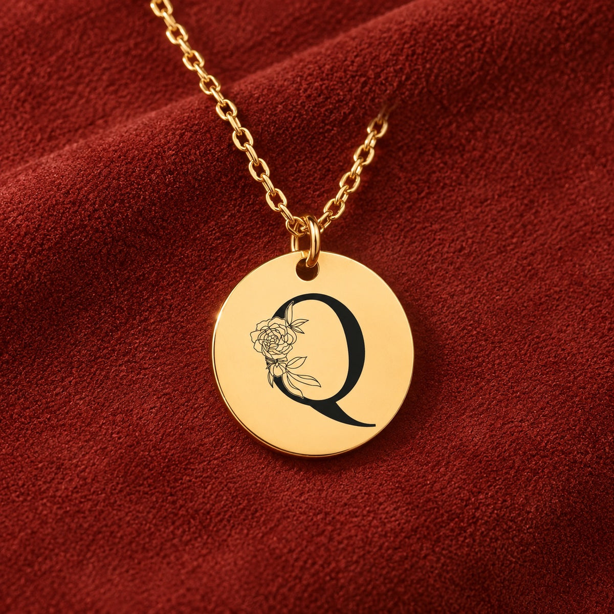 Médaille ronde dorée avec initiale Q et fleurs, sur suédine rouge sanguine.