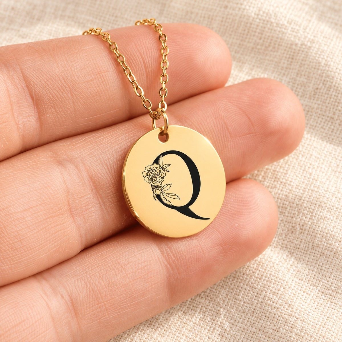Collier initiale florale Q personnalisé doré tenu en main, détail de la gravure.