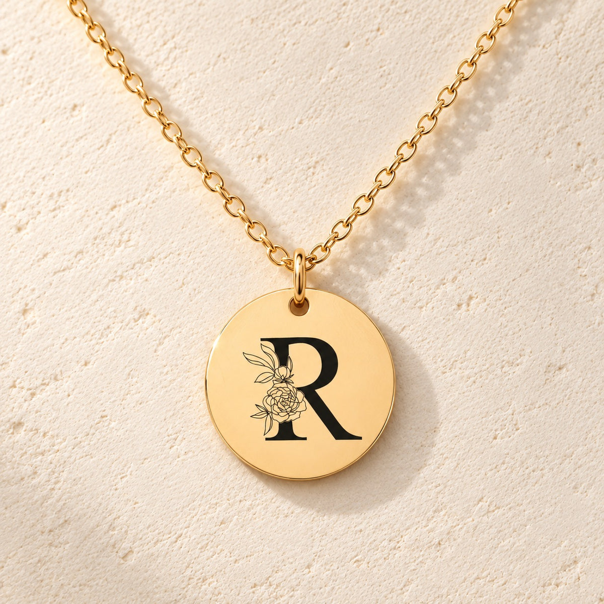 Détail de la médaille ronde dorée avec initiale R et fleurs.