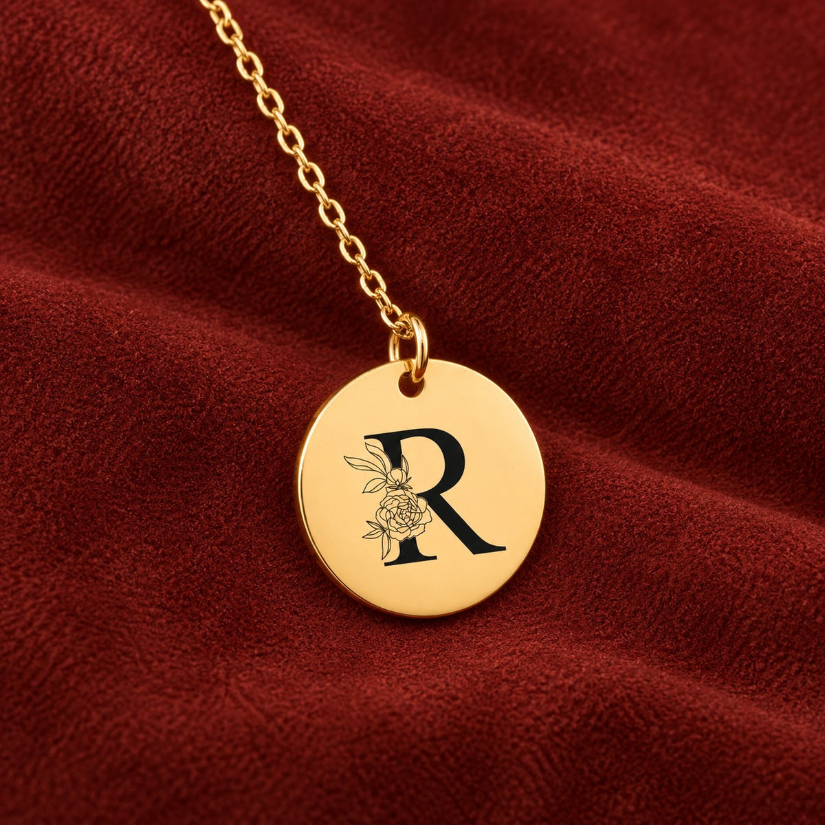 Médaille ronde dorée avec initiale R et fleurs, sur suédine rouge sanguine.