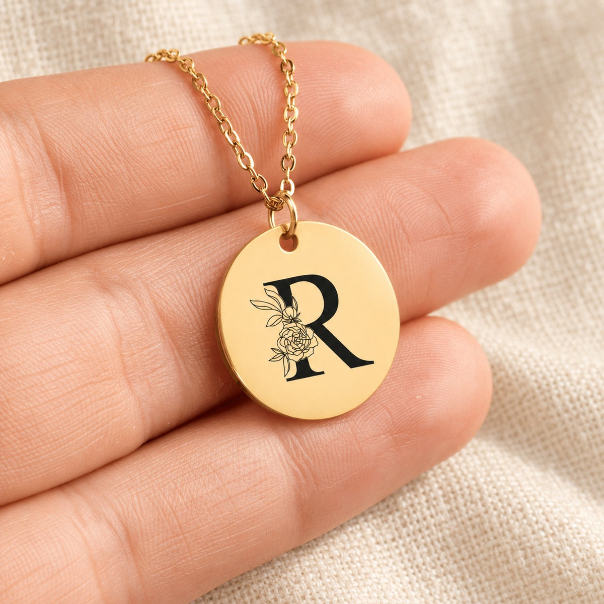 Collier initiale florale R personnalisé doré tenu en main, détail de la gravure.