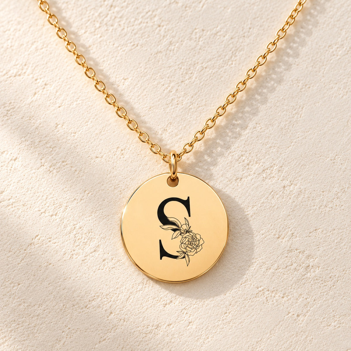 Détail de la médaille ronde dorée avec initiale S et fleurs.
