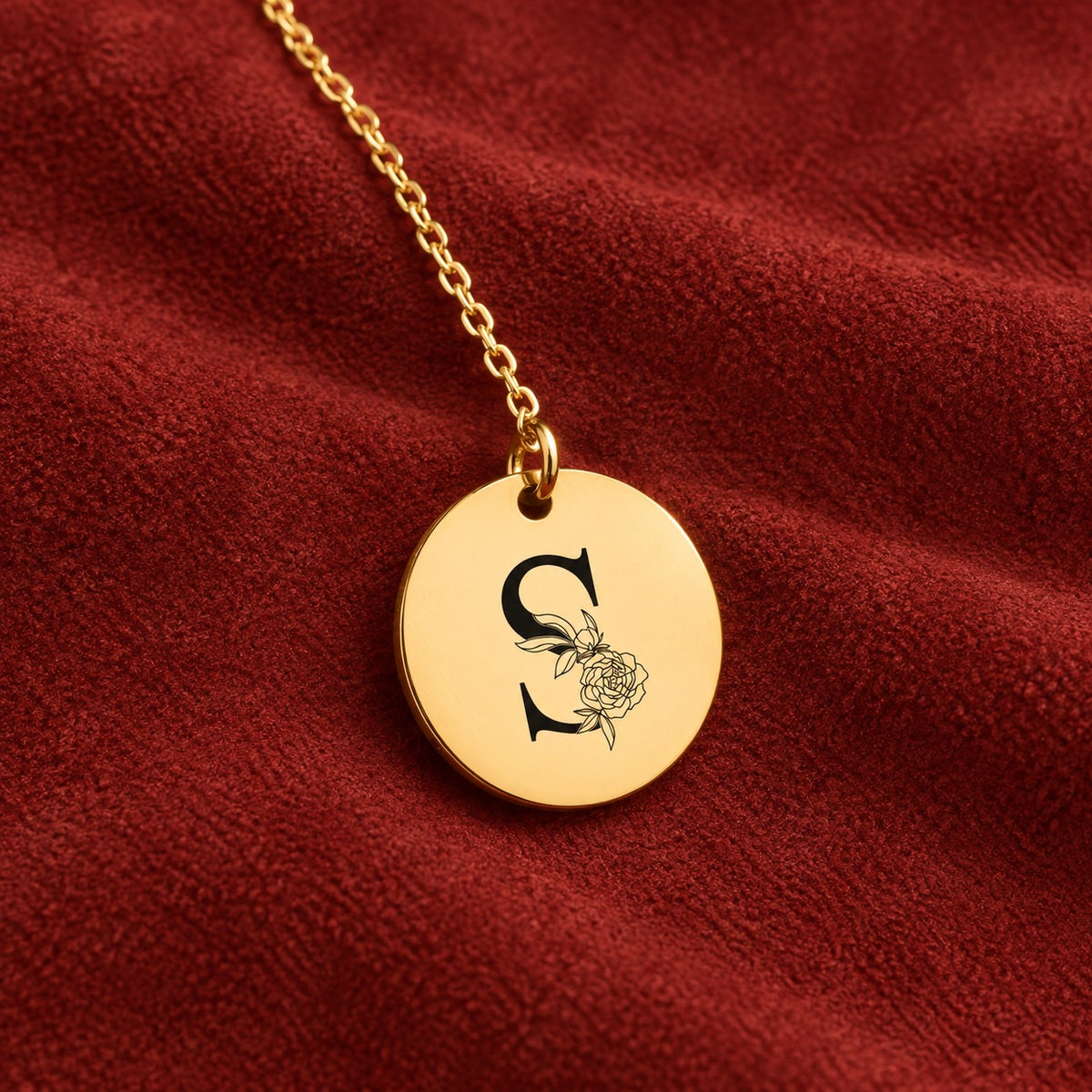 Médaille ronde dorée avec initiale S et fleurs, sur suédine rouge sanguine.