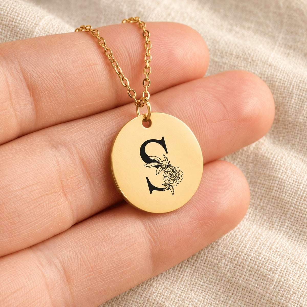 Collier initiale florale S personnalisé doré tenu en main, détail de la gravure.