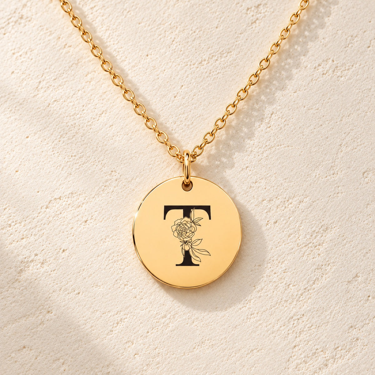 Détail de la médaille ronde dorée avec initiale T et fleurs.