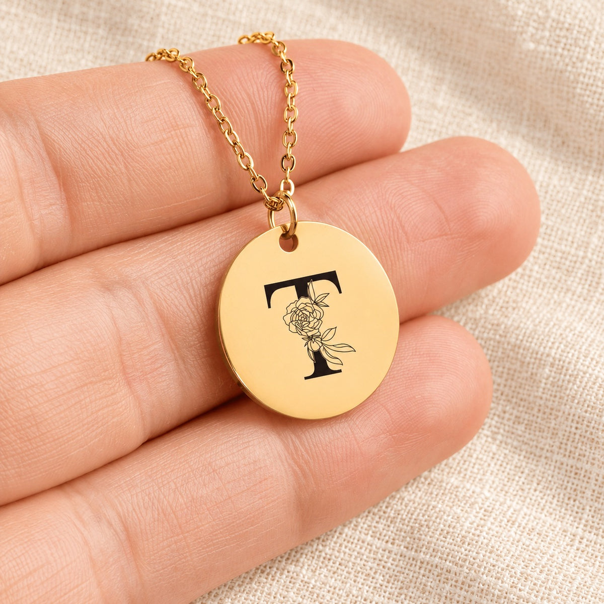 Collier initiale florale T personnalisé doré tenu en main, détail de la gravure.
