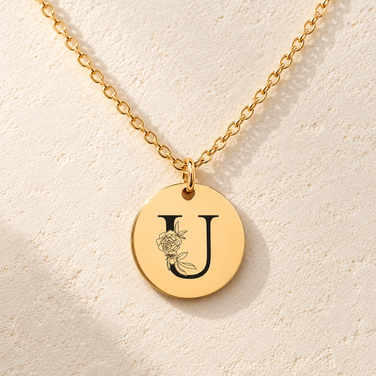 Détail de la médaille ronde dorée avec initiale U et fleurs.