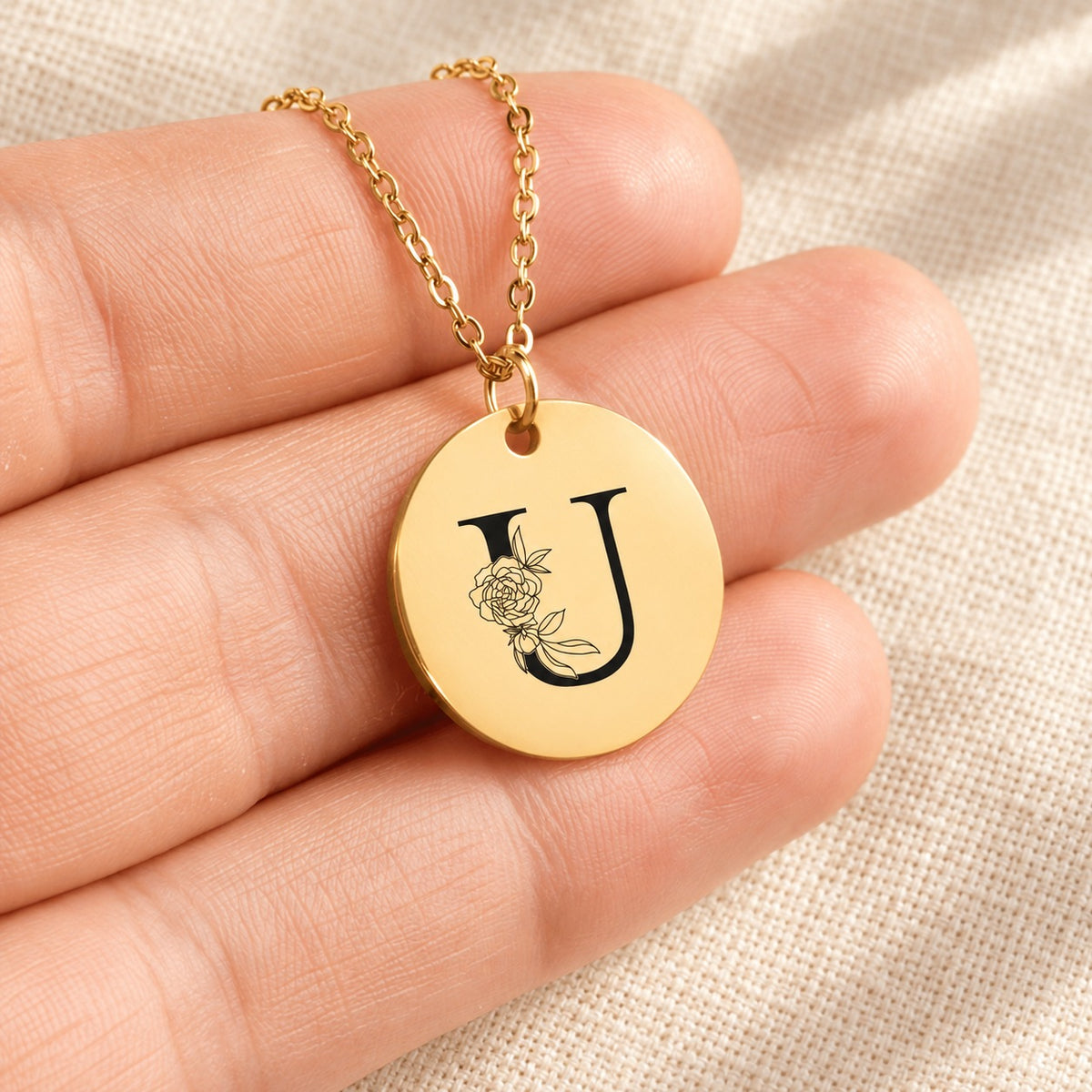 Collier initiale florale U personnalisé doré tenu en main, détail de la gravure.