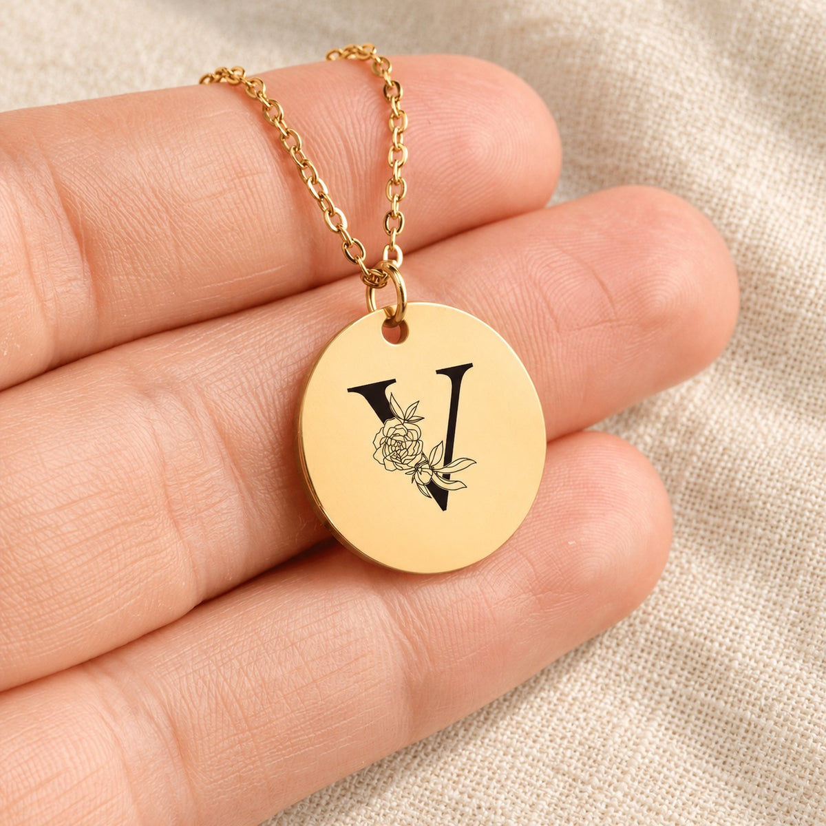 Collier initiale florale V personnalisé doré tenu en main, détail de la gravure.