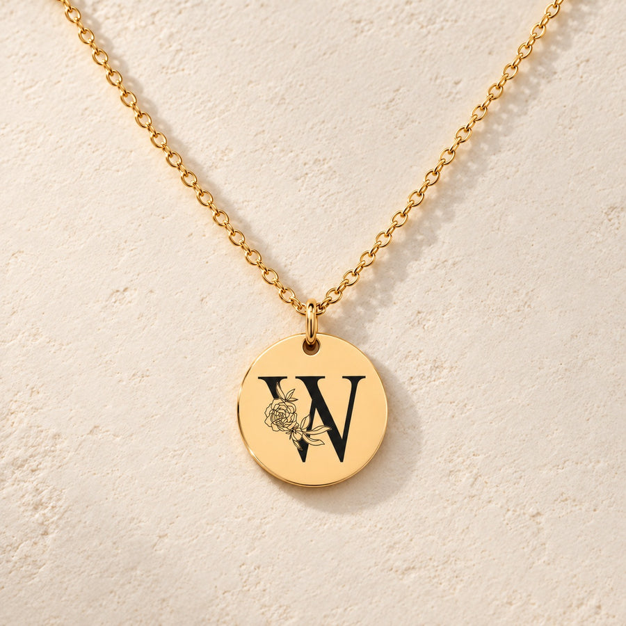 Collier initiale florale W personnalisé doré, médaille ronde gravée avec initiale W et fleurs, sur fond ivoire.