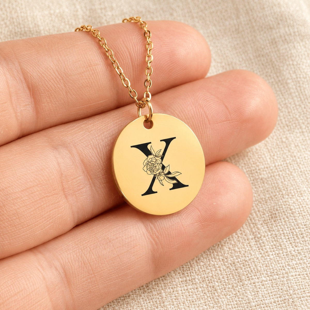 Collier initiale florale X personnalisé doré tenu en main, détail de la gravure.