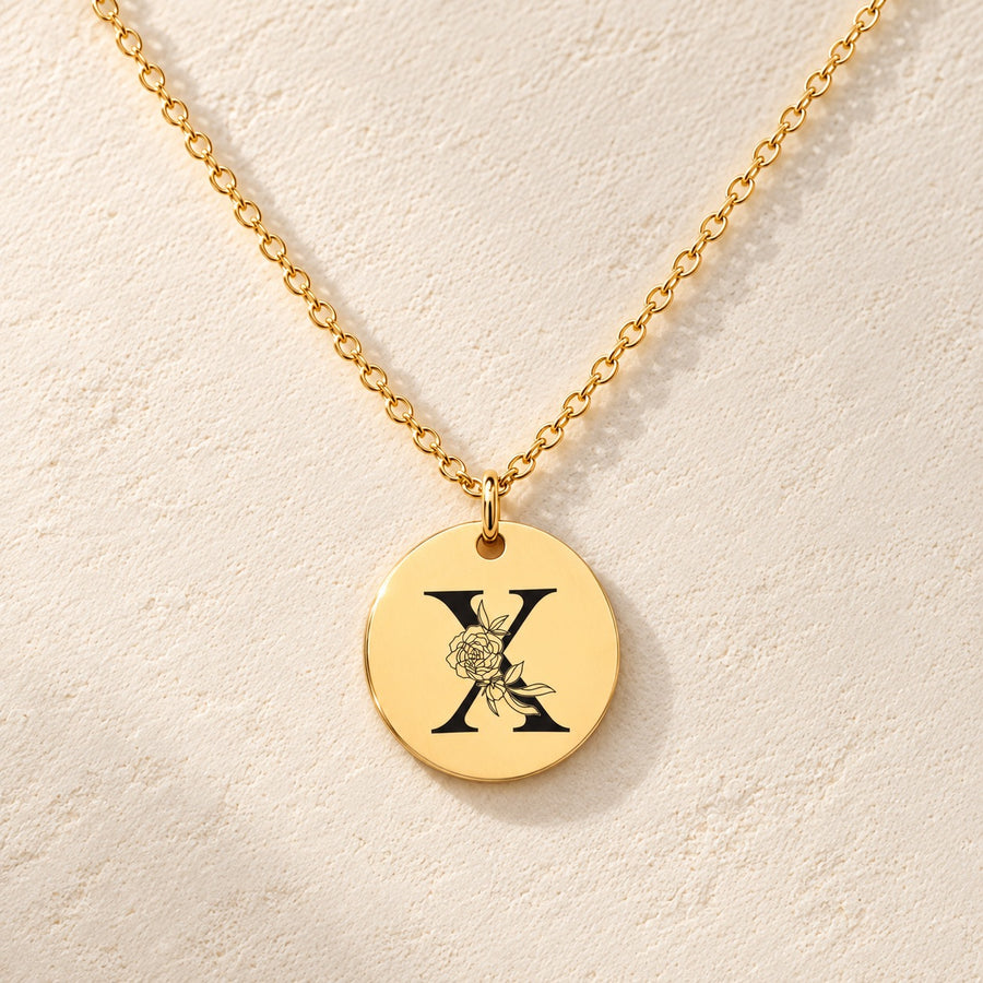 Collier initiale florale X personnalisé doré, médaille ronde gravée avec initiale X et fleurs, sur fond ivoire.