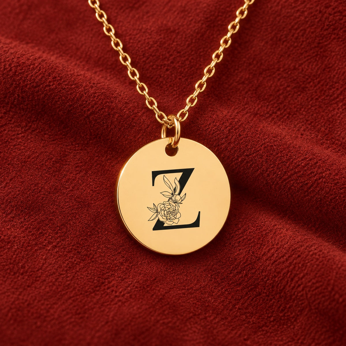 Médaille ronde dorée avec initiale Z et fleurs, sur suédine rouge sanguine.
