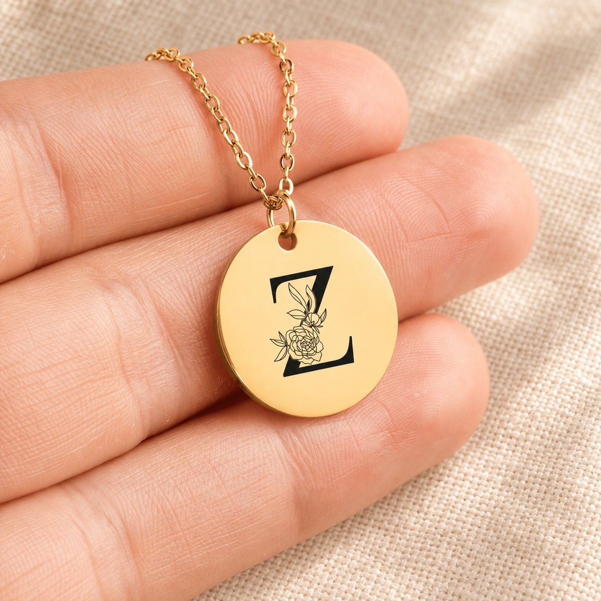 Collier initiale florale Z personnalisé doré tenu en main, détail de la gravure.